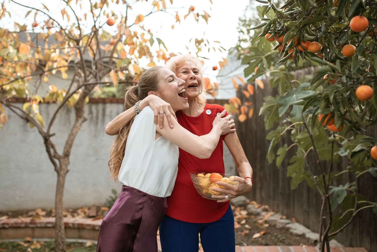 An adult daughter joyfully hugging her mother in a sunlit orchard
