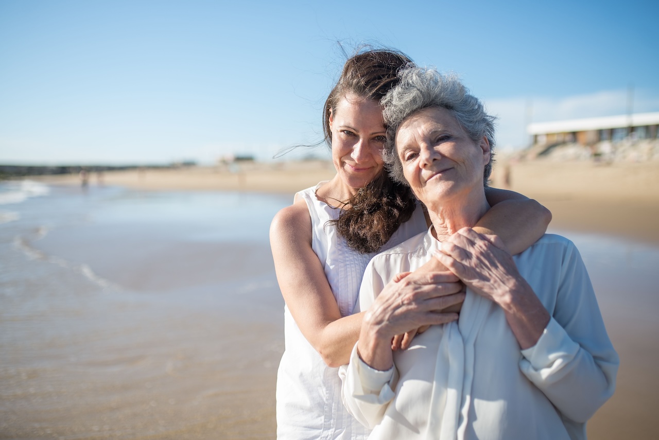 Adult daughter embracing her elderly mother on a sunlit beach